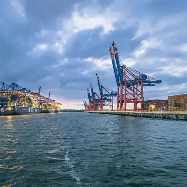 Container port with cargo ships and cranes under cloudy skies.