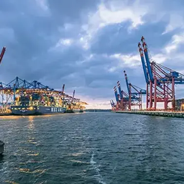Container port with cargo ships and cranes under cloudy skies.