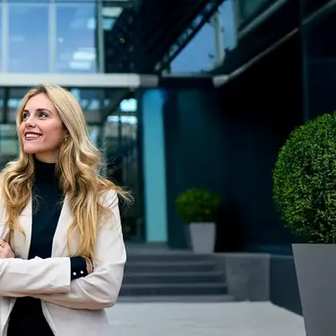 Smiling woman standing outside an office building with crossed arms.